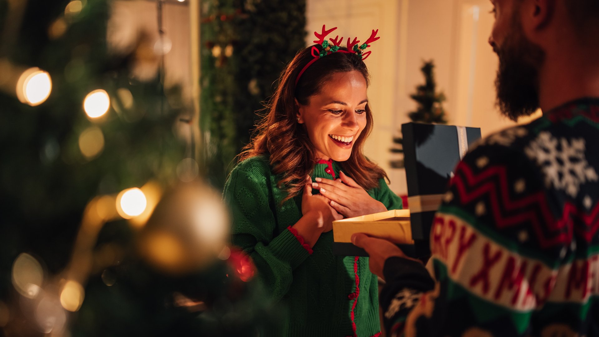 Eine Frau freut sich im Weihnachtsoutfit über ein Geschenk von einen Mann