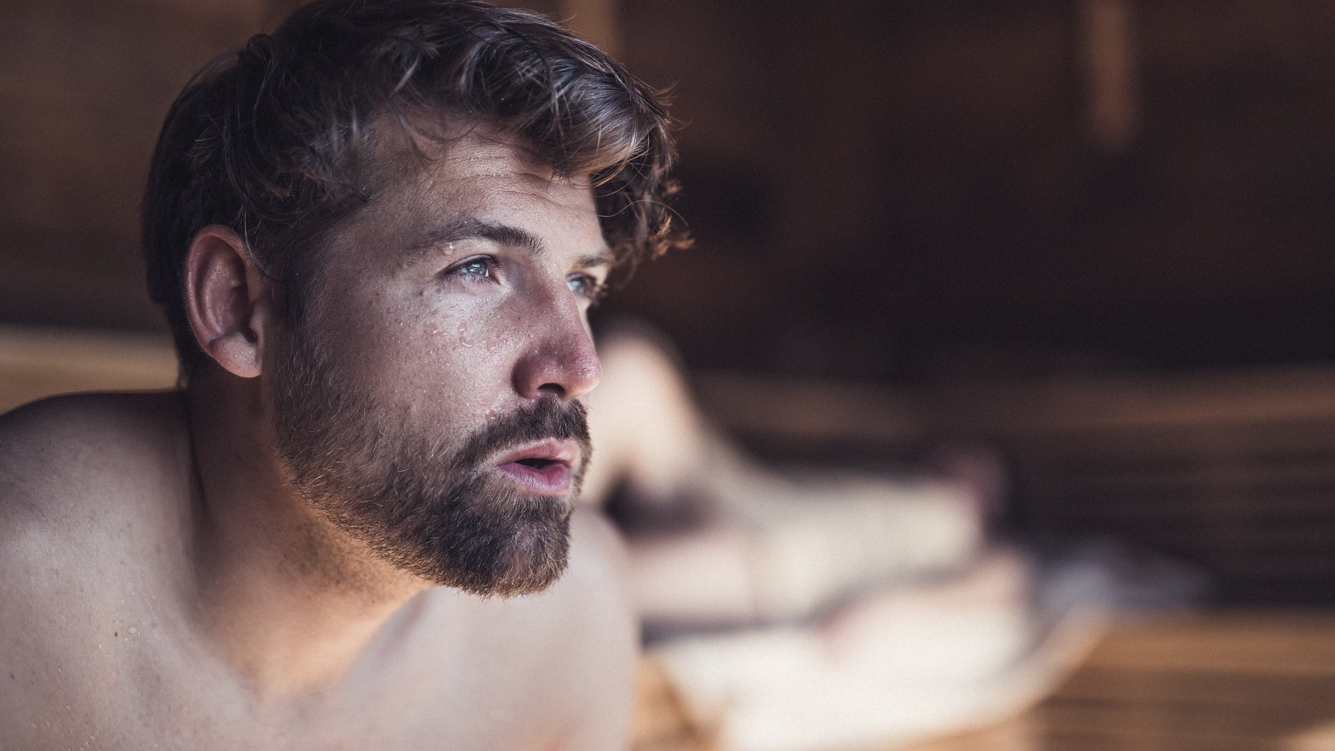 Junger Mann mit Bart schwitzt in der Sauna