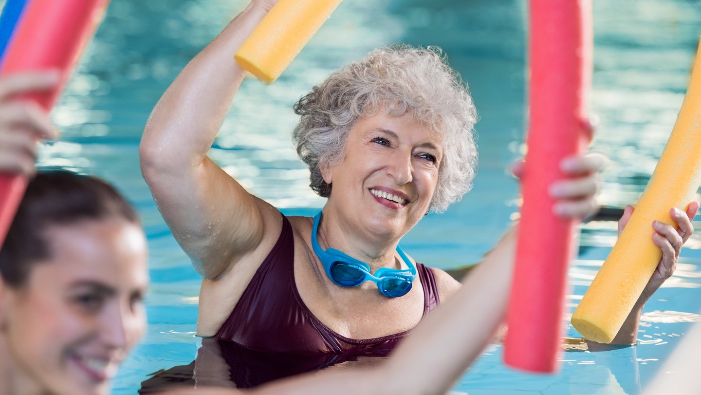 Frau im Seniorenalter mit Poolnudel im Schwimmbecken