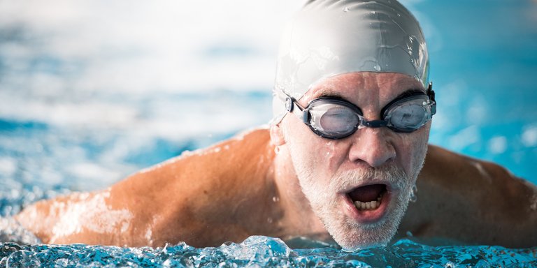 Mann im Seniorenalter schwimmt mit Schwimmbrille und Badekappe